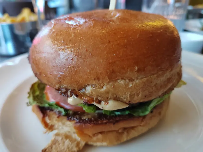 Juicy gourmet burger with brioche bun, lettuce, tomato, and mayo served on a white plate at a restaurant