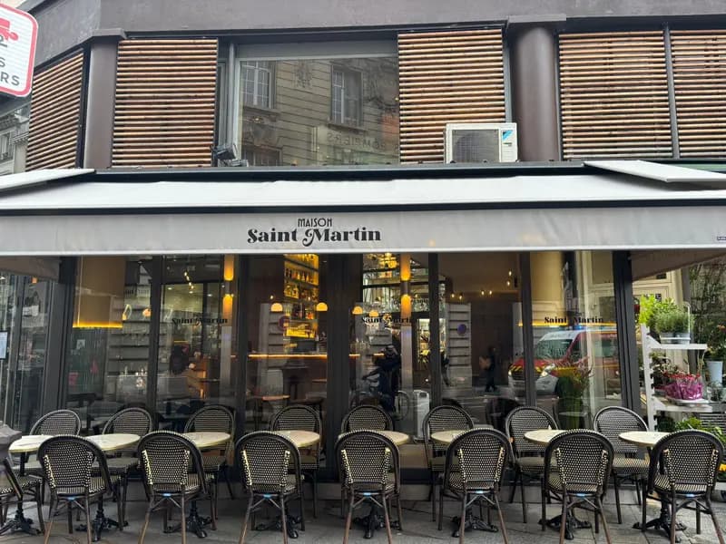 Maison Saint Martin Parisian café exterior with wicker bistro chairs, terrace seating, and warm glowing interior bar