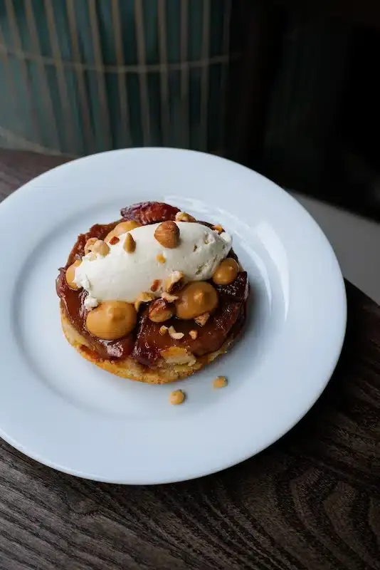 Caramelized apple tatin tart topped with vanilla ice cream and toasted hazelnuts on a white plate