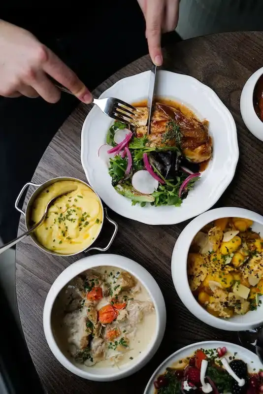 Elegant restaurant table spread with roasted chicken, creamy polenta, potato curry, and white sauce dishes served family-style