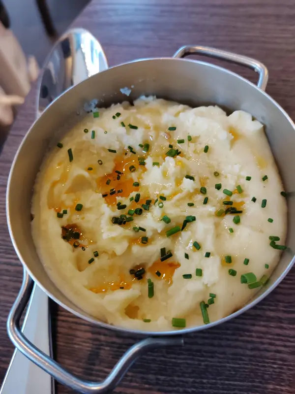 Creamy mashed potatoes topped with melted butter and fresh chives, served in a rustic mini silver pot