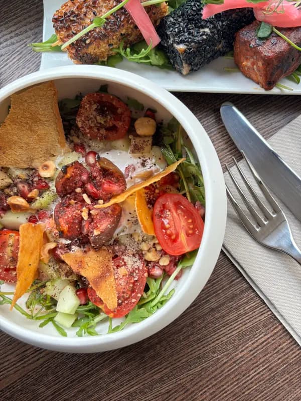 Fresh fig and tomato salad bowl with pomegranate, arugula, crispy chips, and sesame-crusted appetizers at a restaurant.