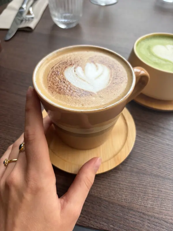 Cappuccino with heart latte art on wooden saucer beside matcha latte at café table