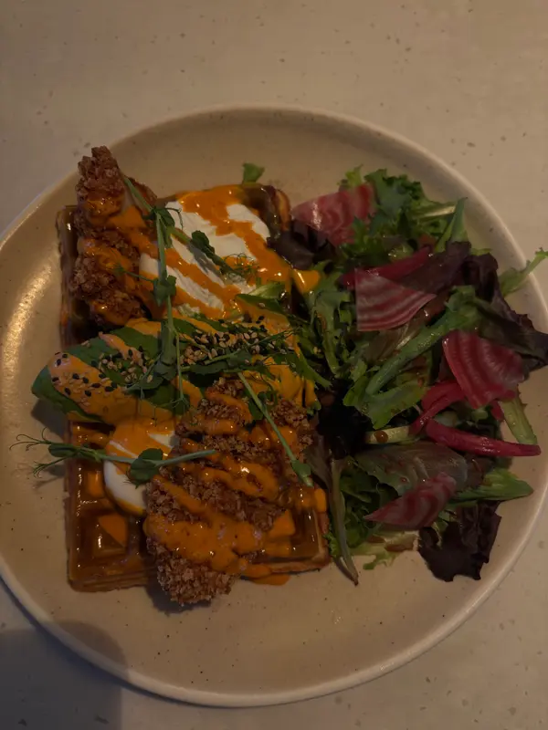 Crispy fried chicken and waffles with spicy orange sauce, poached egg, sesame seeds, microgreens, and pickled beet salad.