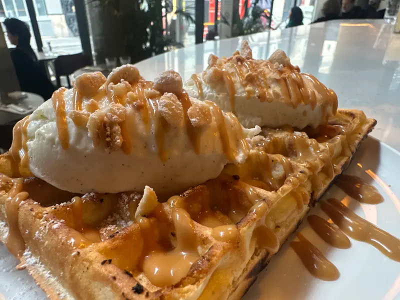 Golden Belgian waffles topped with vanilla ice cream, caramel drizzle, and cookie crumble served on a white plate