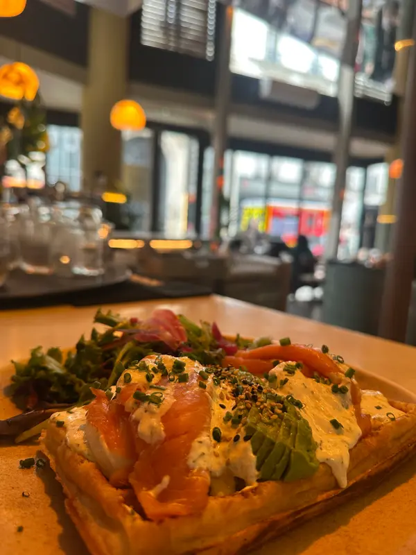 Smoked salmon avocado tart with cream cheese, chives, and sesame seeds, served with mixed greens in a warm café setting.