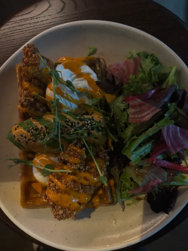 Savory waffle topped with poached eggs, crispy breading, sriracha aioli, sesame seeds, and mixed greens salad with beets.