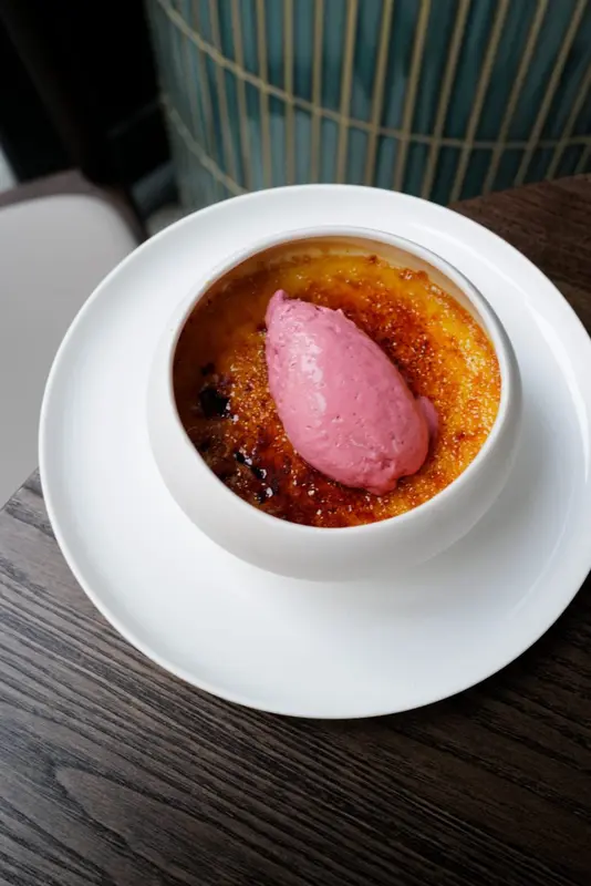 Crème brûlée with pink berry sorbet quenelle in white ramekin, served at upscale restaurant table
